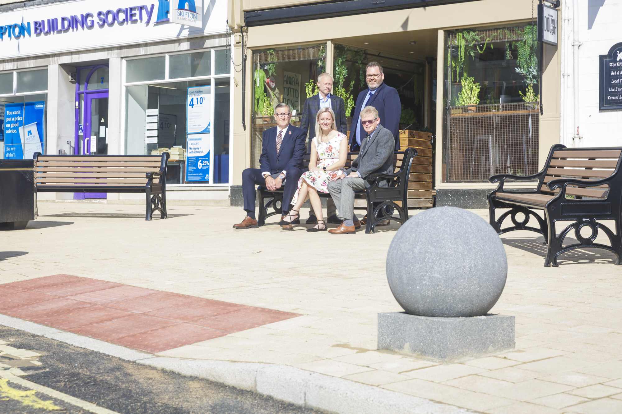 Several people responsible for the improvements to Market Place sat on a bench. Shows the progress made to Market Place Clitheroe