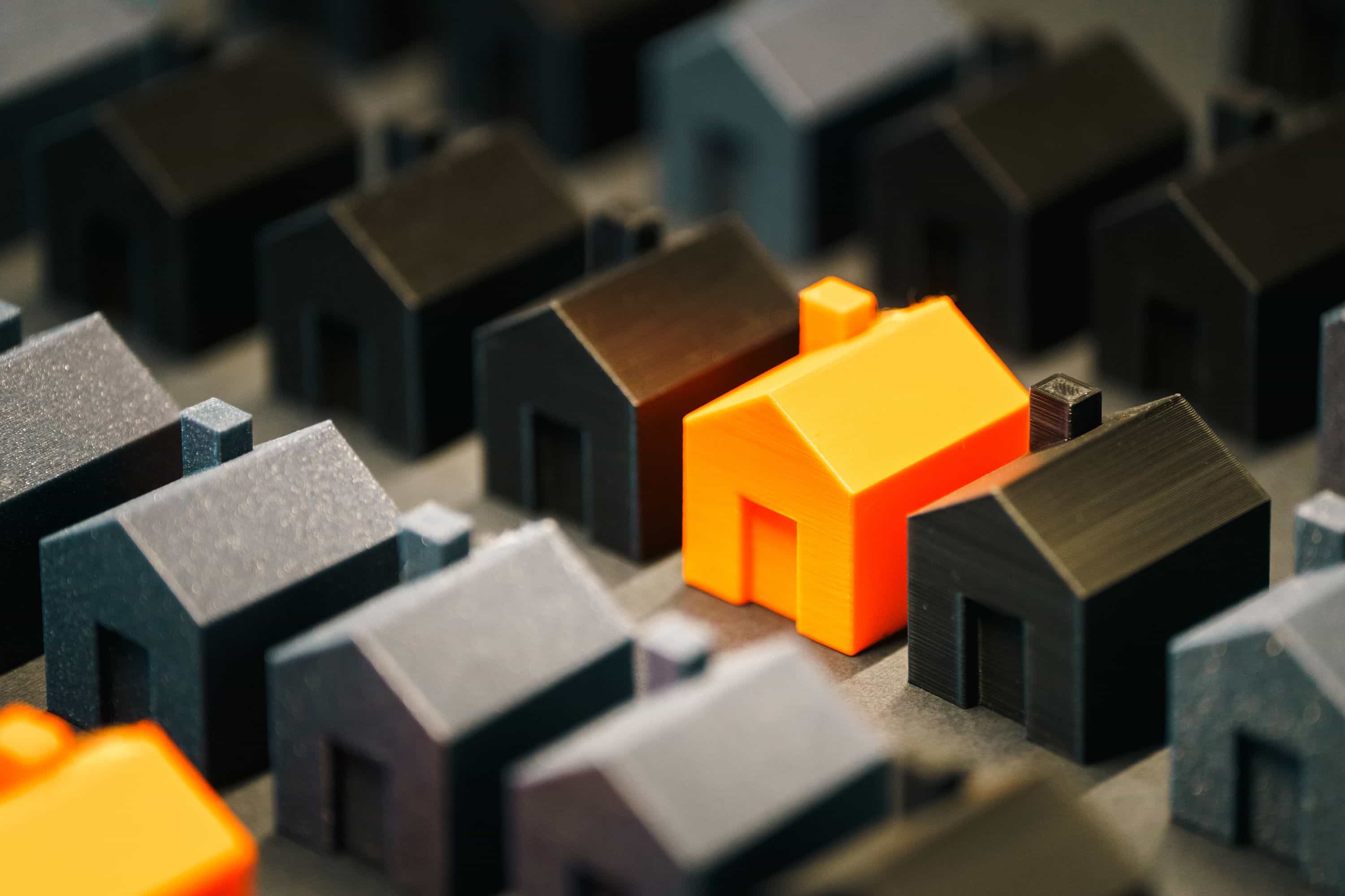 A small orange plastic house in a street of small black plastic houses.