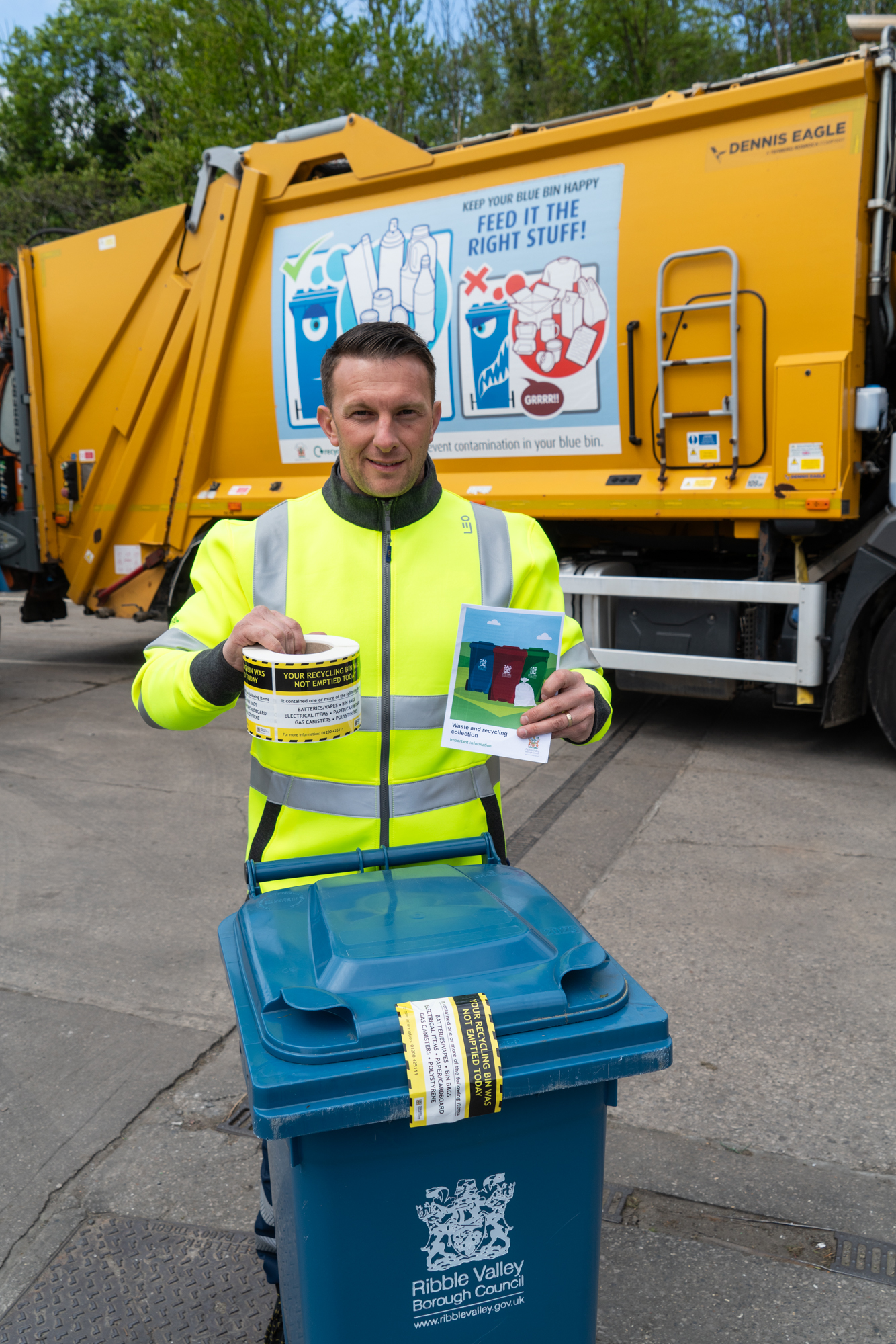 A bin man holding up warning stickers beside a recycling bin