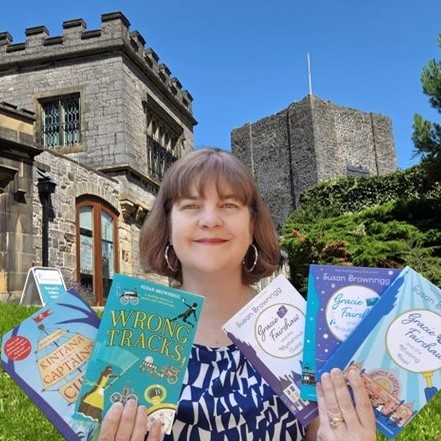 Author Susan Brownrigg holding 5 of her books and stood in front of Clitheroe Castle