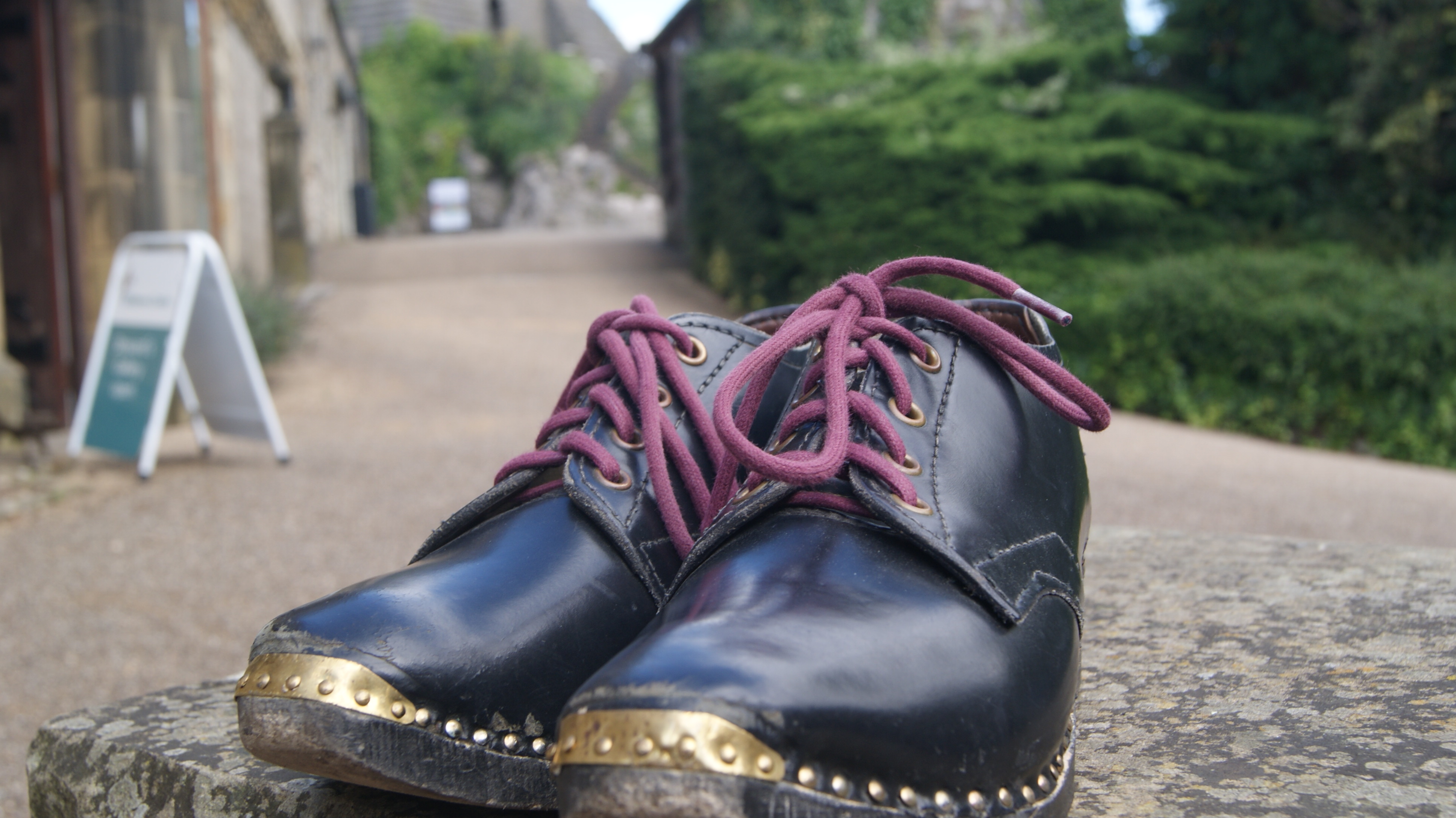 A paid of shiny black clogs on the ground.