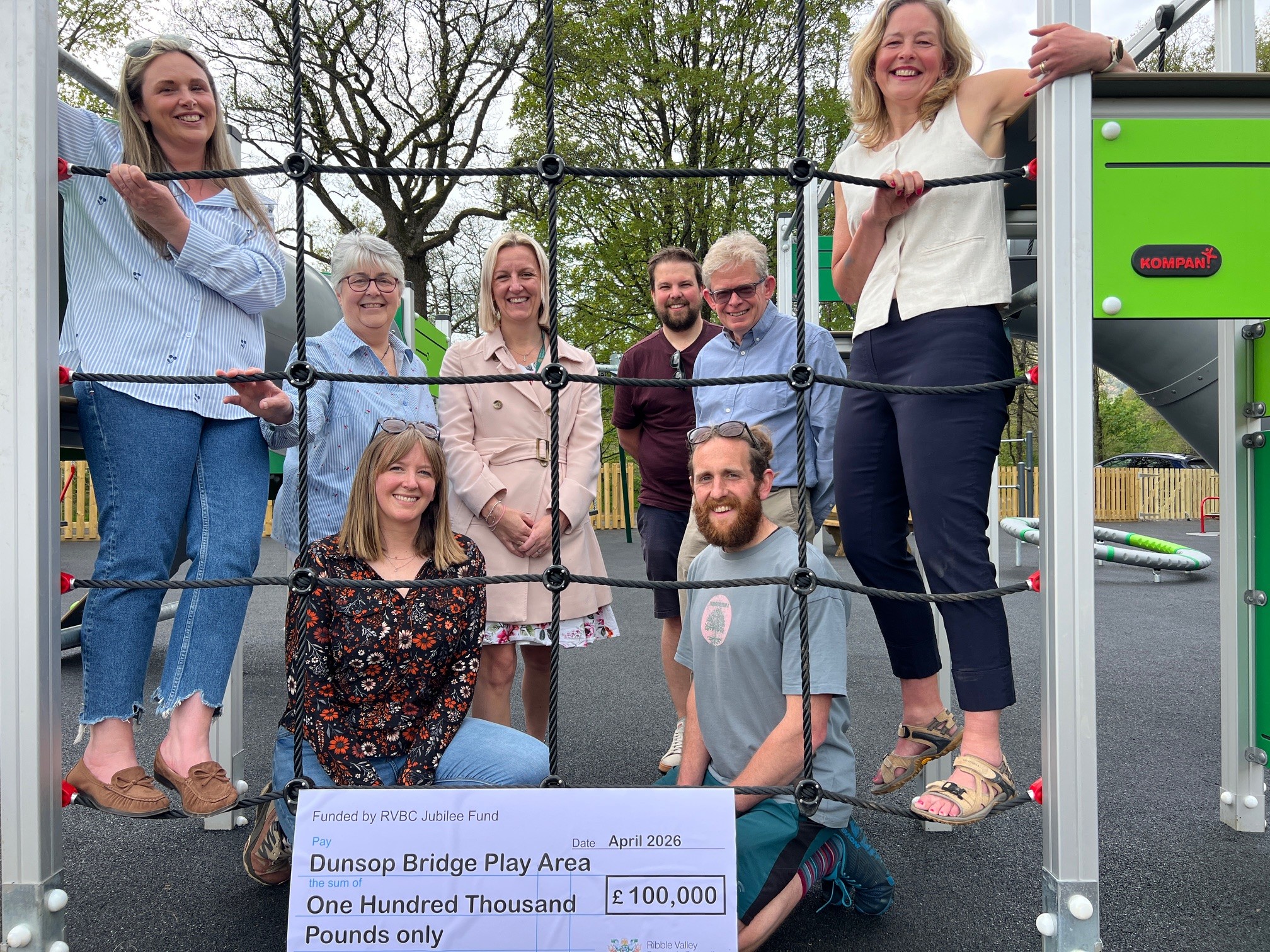 Several smiling people stood behind climbing netting on a playground