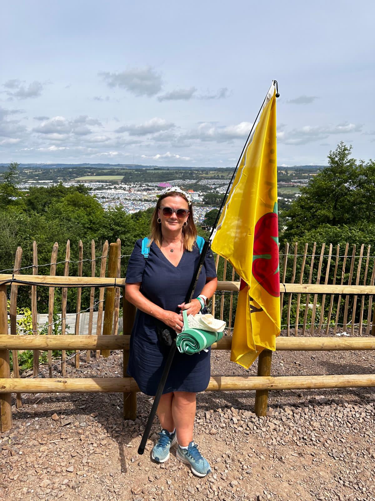 Former director of resources Jane Pearson stood with a Lancashire red rose flag with Glastonbury festival crowds in the distance.