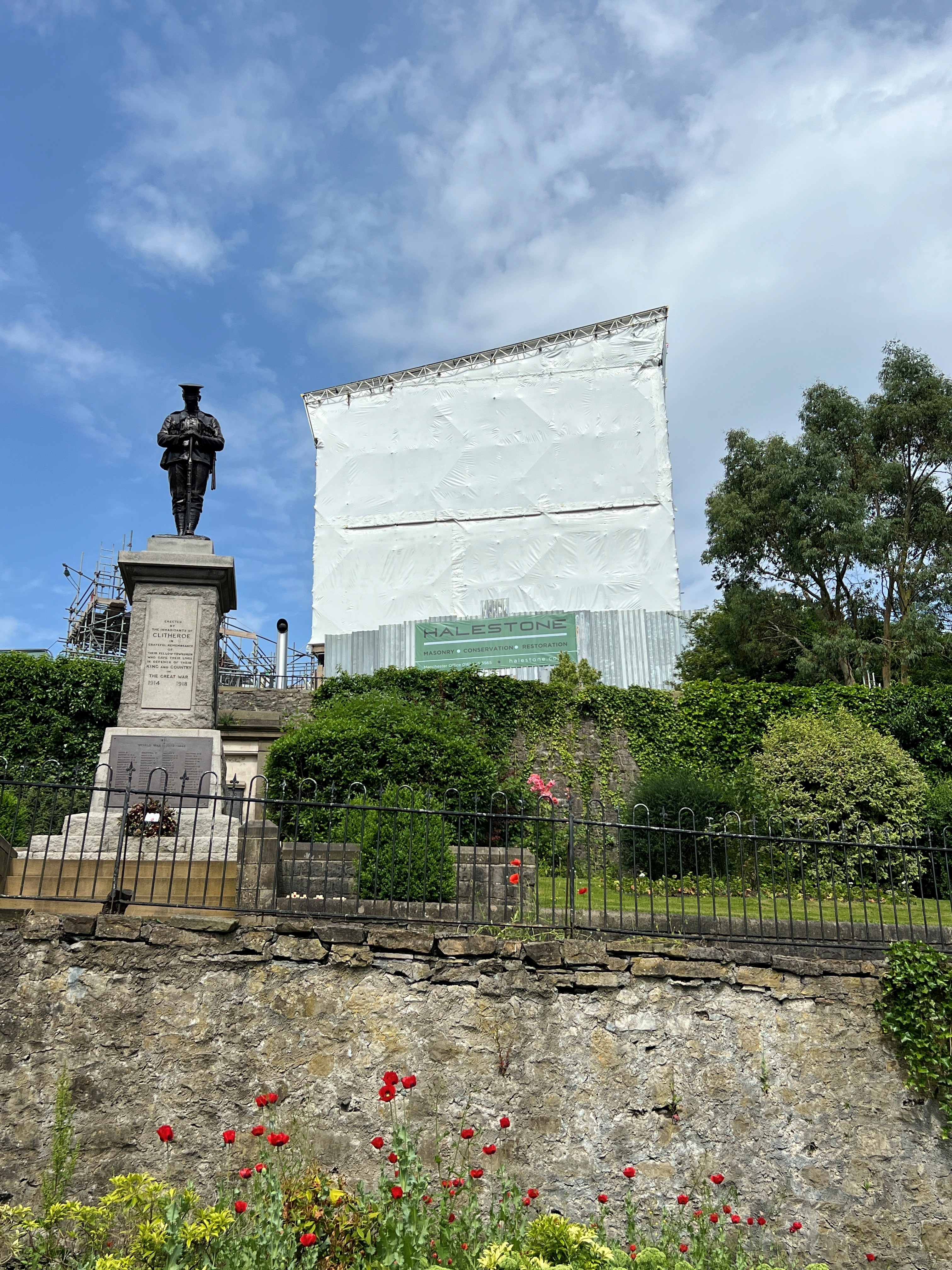 A large white tarp covering Clitheroe Castle. The war memorial is visible in the foreground.