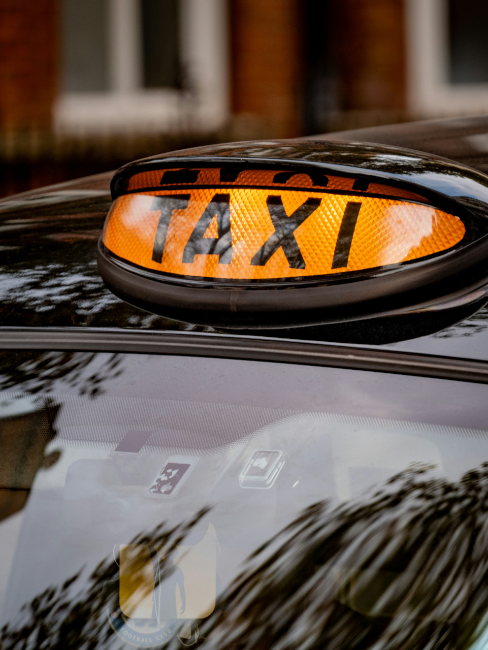 A lit up taxi sign on the roof of a black cab